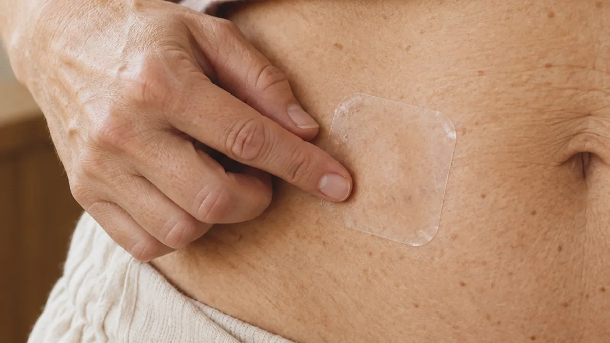 A hand pressing a patch onto the lower abdomen